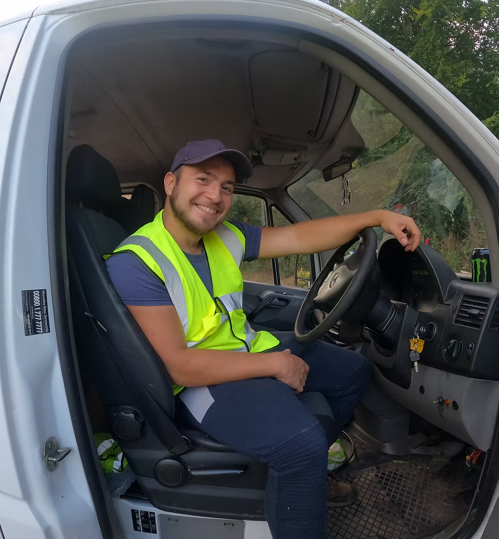 Matt, founder of Take Me Elsewhere, smiling behind the wheel of a company van wearing a hi-vis vest