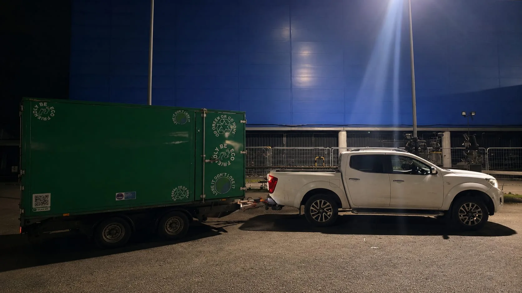 Pickup towing a green welfare trailer at a film unit base at night